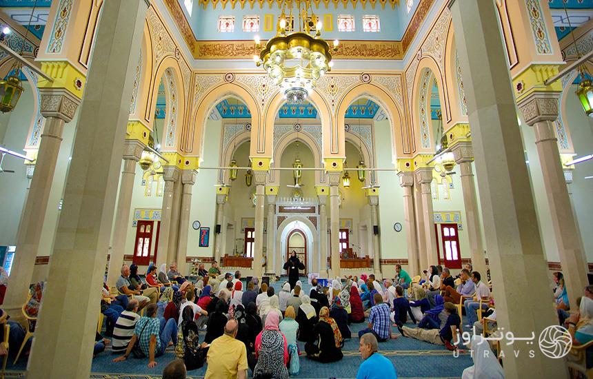 تصویری از فضای داخلی مسجد جمیرای دبی که جمعیتی از مردان و زنان را نشسته در داخل مسجد نشان می‌دهد